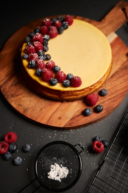 Photo gratuite tir vertical d'un gâteau au fromage avec des baies sur le dessus sur une plaque en bois