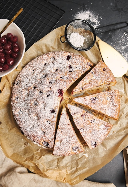 Photo gratuite tir vertical d'un gâteau aux cerises avec du sucre en poudre et des ingrédients sur le côté sur fond noir