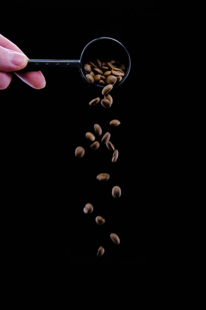 Tir vertical de grains de café tombant d'une cuillère à café isolée sur fond noir