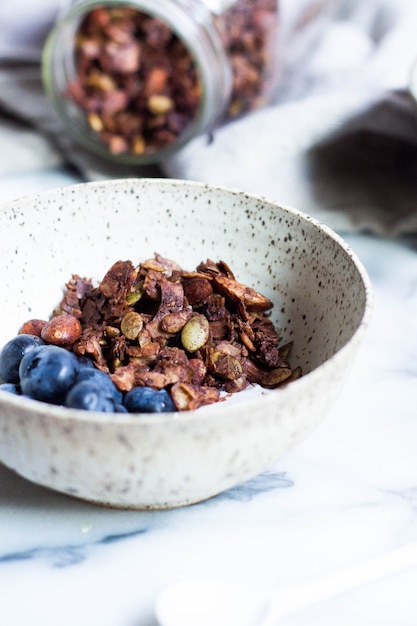 Tir vertical de granola cacao paléo et myrtilles dans un bol blanc avec un arrière-plan flou