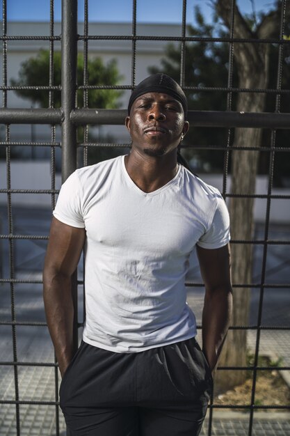 Tir vertical d'un homme afro-américain dans une chemise blanche s'appuyant sur une clôture