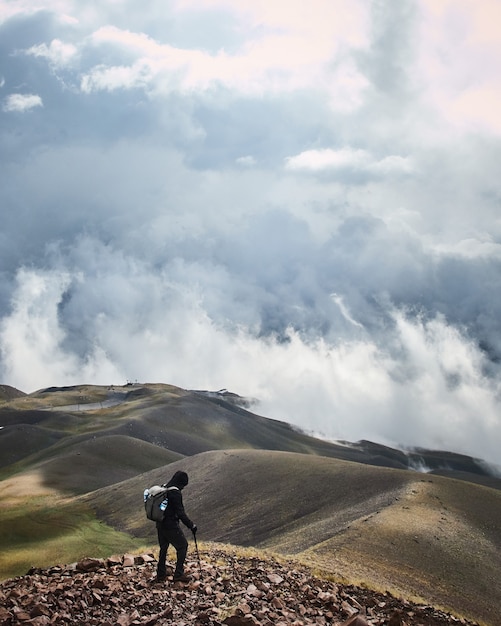 Tir vertical d'un homme debout sur une montagne avec un ciel nuageux en arrière-plan