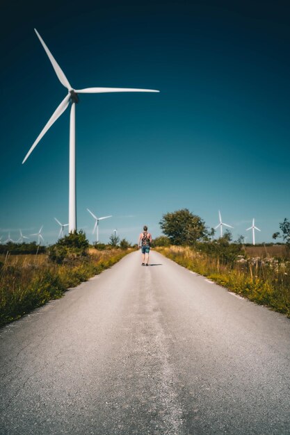 Tir vertical d'un homme marchant sur la route avec des éoliennes sur le bord de la route