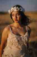 Photo gratuite tir vertical d'une jeune femme de race blanche en robe blanche et couronne de fleurs blanches posant dans un champ