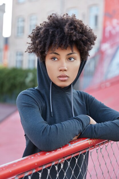 Tir vertical d'une jolie femme à la peau foncée avec coupe de cheveux afro, habillée en capuche