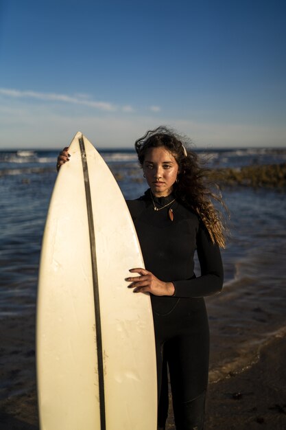 Tir vertical d'une jolie femme tenant une planche de surf au bord de la mer en Espagne