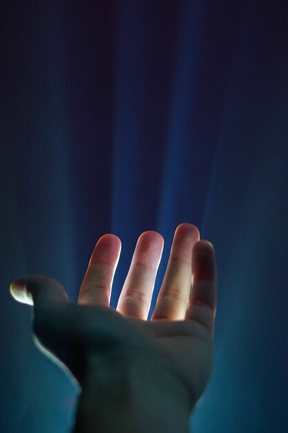 Tir vertical de la main d'une personne avec une lumière qui brille entre les doigts