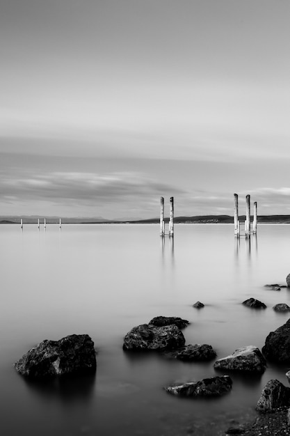 Photo gratuite tir vertical en niveaux de gris d'une jetée en bois près de formations rocheuses sous le ciel nuageux