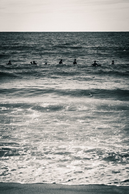 Tir vertical en niveaux de gris d'une mer avec des silhouettes de personnes