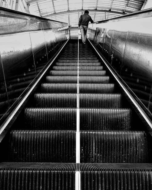 Tir vertical en niveaux de gris d'une personne debout sur un escalator