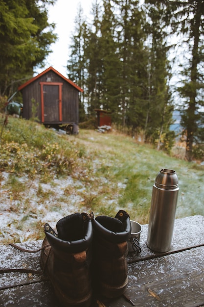 Tir vertical d'une paire de bottes et d'un flacon près d'un chalet en bois dans la forêt en Norvège