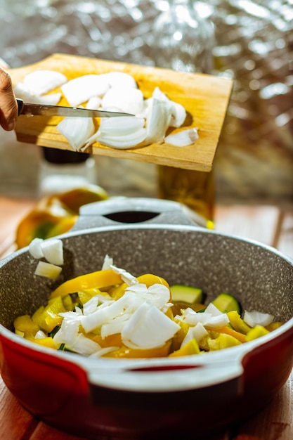 Photo gratuite tir vertical de quelqu'un ajoutant les oignons dans le pot rempli de poivron jaune et de courgette