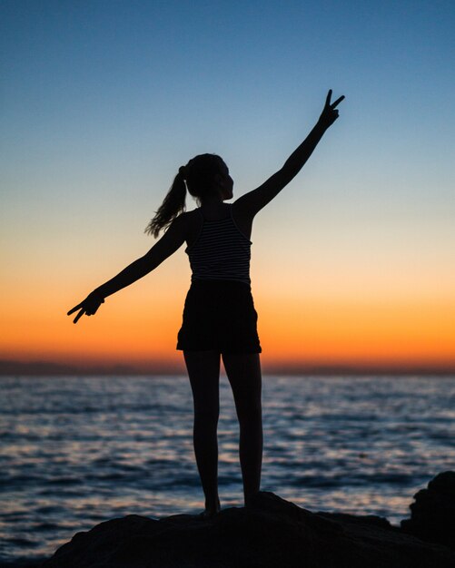 Tir vertical de la silhouette d'une femme avec ses bras ouverts montrant le signe de la victoire