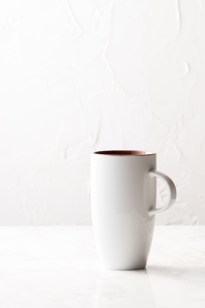 Tir vertical d'une tasse en céramique blanche sur une surface blanche