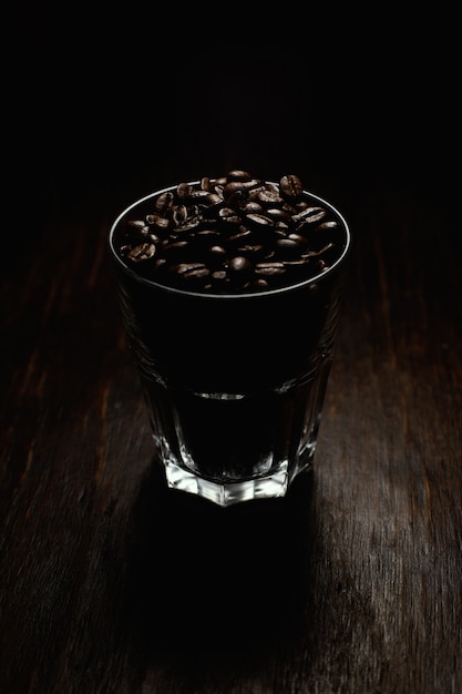 Tir vertical d'une tasse en verre remplie de grains de café sur une surface en bois avec un fond noir