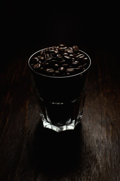 Tir vertical d'une tasse en verre remplie de grains de café sur une surface en bois avec un fond noir