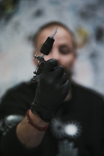 Tir vertical d'un tatoueur professionnel dans des gants en latex noir préparant la machine pour le tatouage