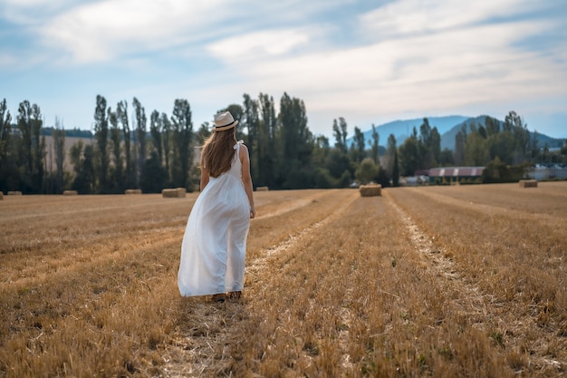 Tiré d'une jeune paysanne attirante dans une robe blanche dans un champ sec de paille