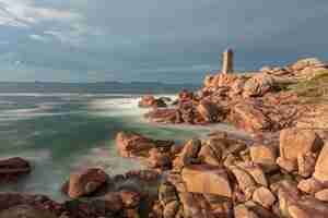 Photo gratuite tiré d'un phare debout au bord de la mer sous le ciel nuageux