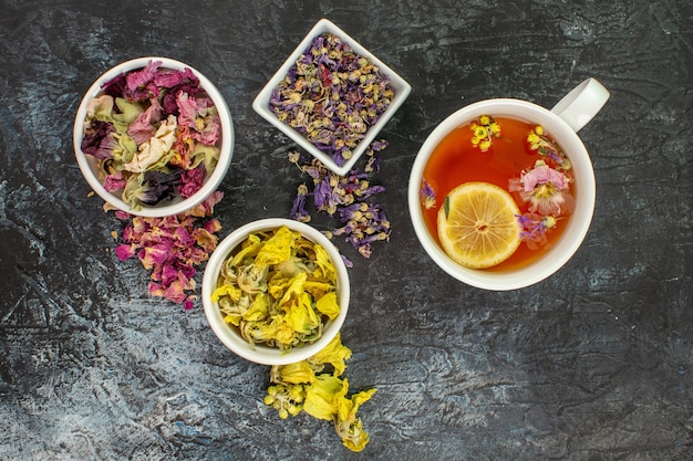 Tisane près de bols de fleurs séchées sur fond gris