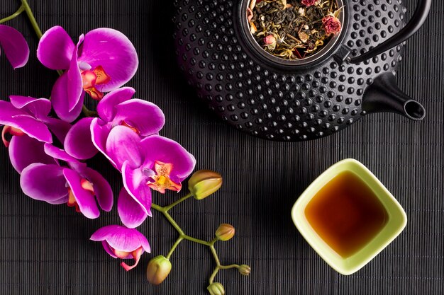 Tisane sèche avec fleur d&#39;orchidée rose et théière sur un napperon noir