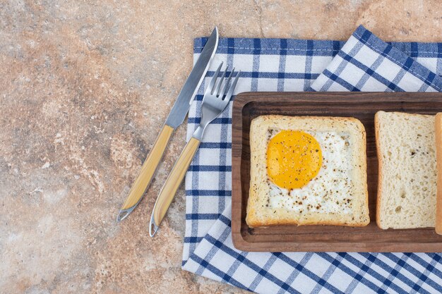 Toast aux œufs avec des épices sur une plaque en bois avec des couverts