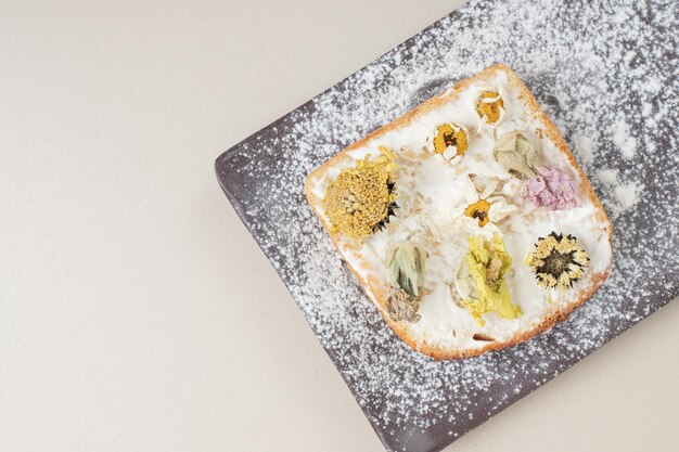 Toast avec des fleurs séchées et de la farine sur une planche à découper foncée.