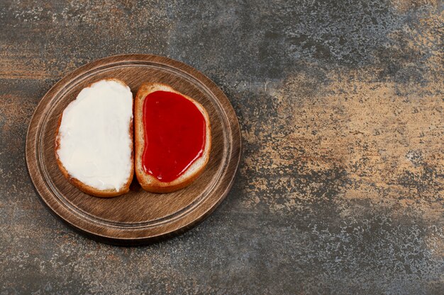 Toasts avec confiture de fraises et crème sure sur planche de bois.