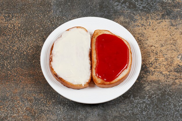 Toasts avec confiture de fraises et crème sure sur plaque blanche.