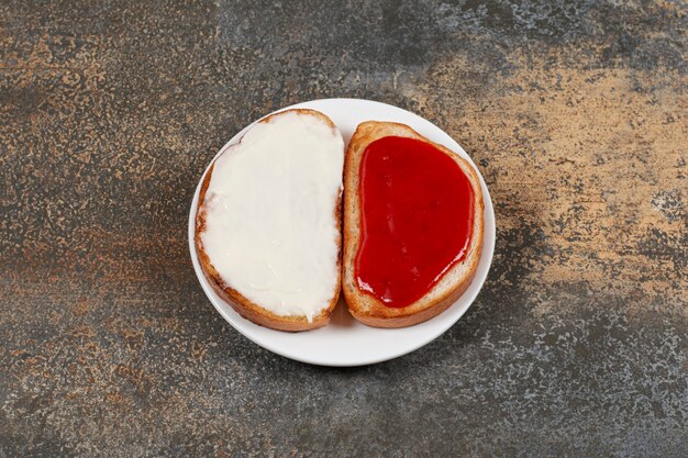 Toasts avec confiture de fraises et crème sure sur plaque blanche.