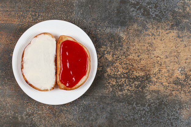 Toasts avec confiture de fraises et crème sure sur plaque blanche.