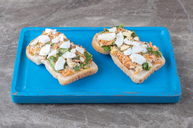 Toasts savoureux avec des légumes tranchés sur plaque bleue.