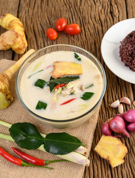 Tom Kha Kai dans un bol avec des feuilles de lime kaffir, de la citronnelle, de l'oignon rouge, du galanga et du piment.