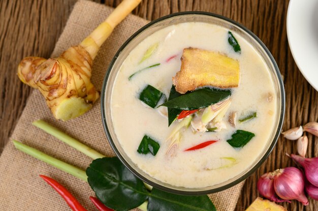 Tom Kha Kai dans un bol avec des feuilles de lime kaffir, de la citronnelle, de l'oignon rouge, du galanga et du piment.