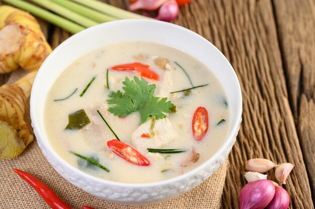 Tom Kha Kai dans un bol avec des feuilles de lime kaffir, de la citronnelle, de l'oignon rouge, du galanga et du piment.