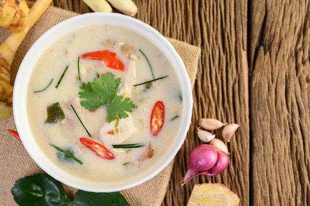 Tom Kha Kai dans un bol avec des feuilles de lime kaffir, de la citronnelle, de l'oignon rouge, du galanga et du piment.