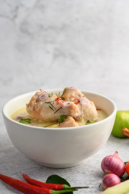 Tom Kha Kai dans un bol avec des feuilles de lime kaffir, de la citronnelle, de l'oignon rouge, du galanga et du piment.