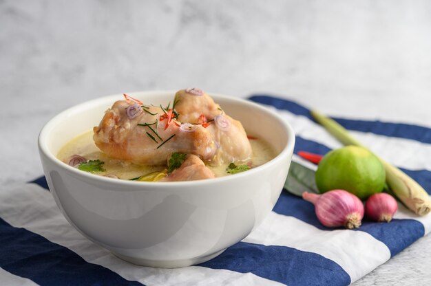 Tom Kha Kai dans un bol avec des feuilles de lime kaffir, de la citronnelle, de l'oignon rouge, du galanga et du piment.