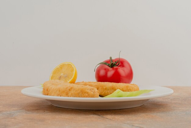 Tomate, citron, pépites de poulet sur plaque blanche.