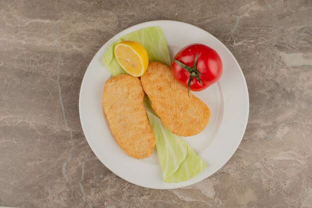 Tomate, citron, pépites de poulet sur plaque blanche.