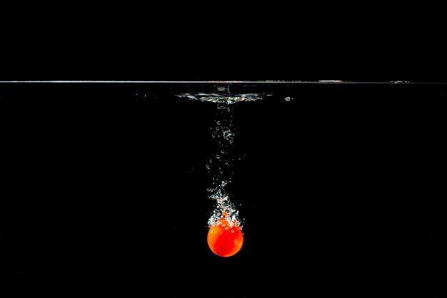 Tomate fraîche tombant dans l&#39;eau claire sur fond noir