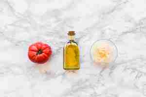 Photo gratuite tomate rouge avec une bouteille d'huile d'olive et fromage râpé dans un bol sur toile de fond en marbre blanc