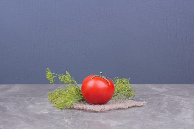 Tomate unique sur marbre aux herbes.