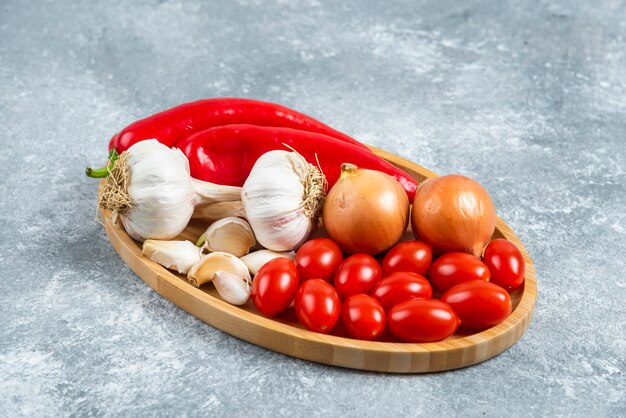 Tomates, ail et poivrons sur plaque en bois.