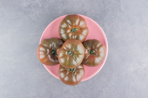 Tomates appétissantes dans l'assiette, sur la surface en marbre