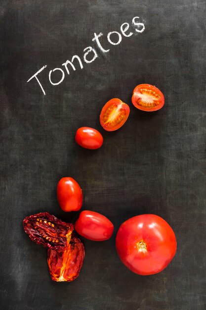 Tomates biologiques séchées et fraîches sur tableau noir par dessus tableau noir