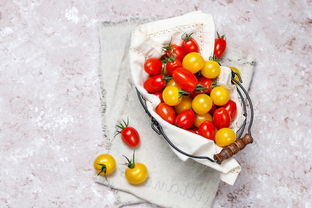 Tomates cerises de différentes couleurs, tomates cerises jaunes et rouges dans un panier sur fond clair