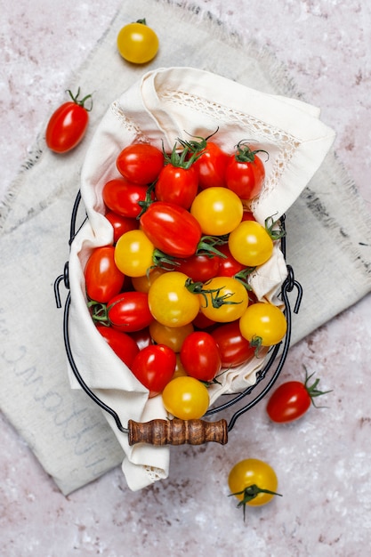 Tomates cerises de différentes couleurs, tomates cerises jaunes et rouges dans un panier sur fond clair