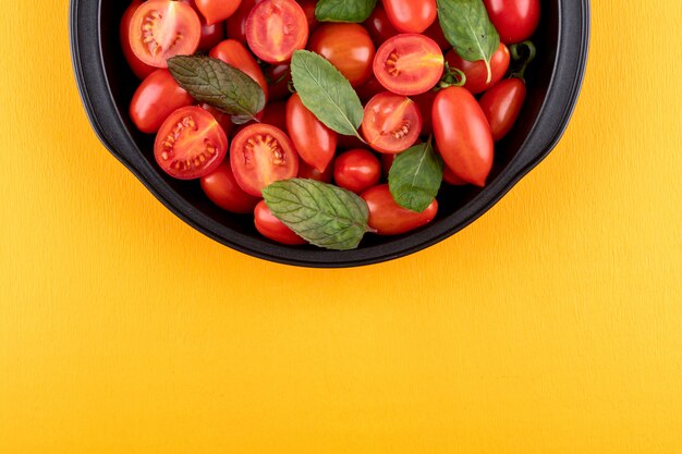 Tomates cerises et feuilles de menthe dans un bol noir sur la surface jaune vue de dessus avec copie espace