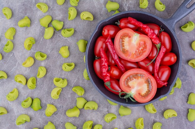 Photo gratuite tomates cerises et piments rouges dans une poêle noire avec des pâtes vertes autour.